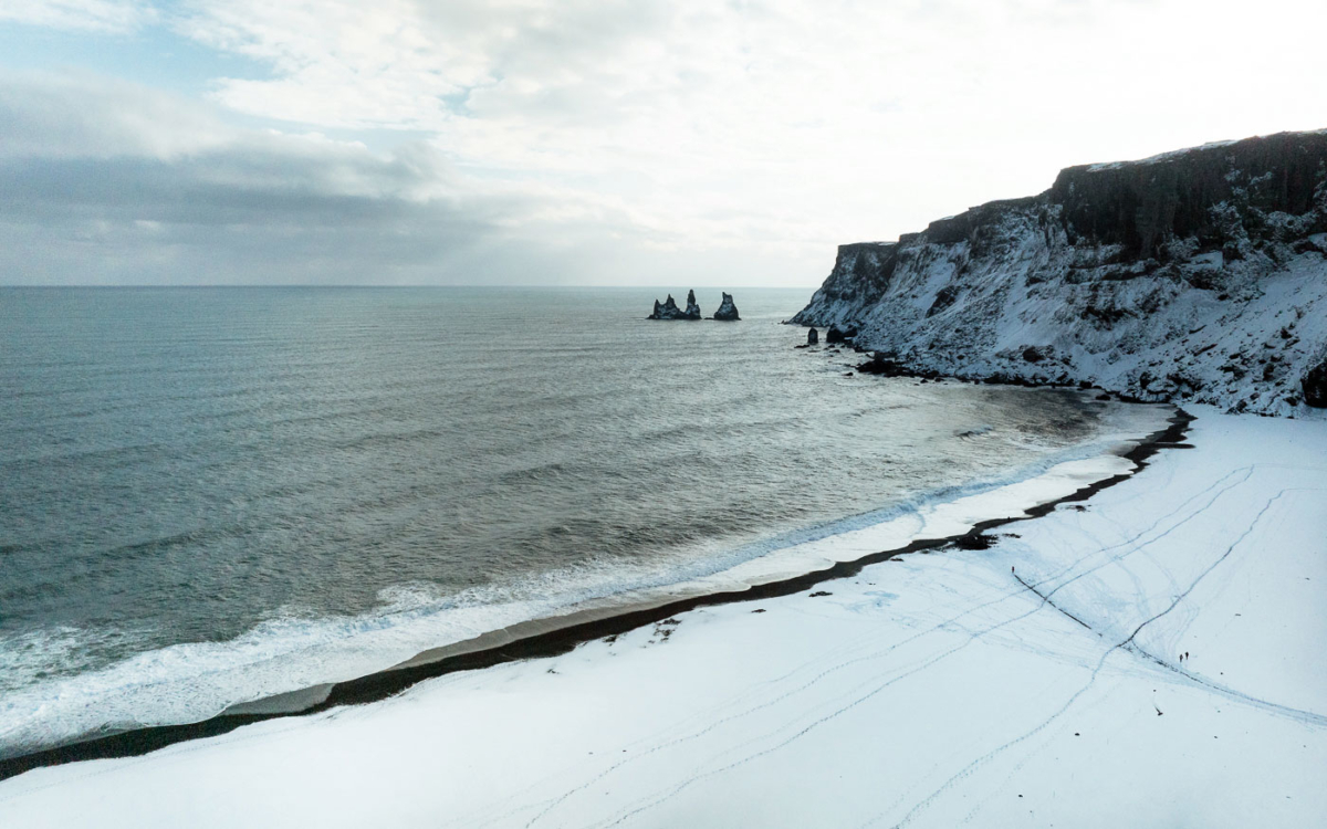 Schwarzer Strand in Vik mit Blick auf die bekannten Basaltsäulen mit Schnee